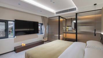 A modern hotel room with a large bed, a flat-screen TV, a bathroom with a mirror, and a window with curtains.