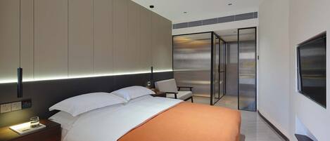 Ein modernes Hotelzimmer mit Bett, Nachttisch, Sessel und Fernseher.