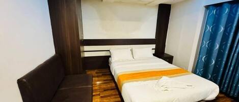Ein Hotelzimmer mit einem Bett, einem blauen Sessel, Holzboden und einem fenster mit Vorhängen.