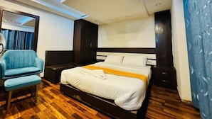 A hotel room with a large bed, a blue armchair, a wooden floor, and a ceiling with recessed lighting. - Hotel Dhaka Express (Kathmandu)