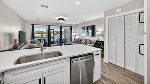 A modern kitchen with a dishwasher, a sink, and a dining area with a view. - Barefoot Bliss | Lakefront Villa Steps from Miramar Beach (Miramar Beach)