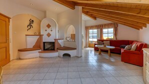 Una sala de estar con chimenea, un sofá rojo, vigas de madera y piso de baldosas.