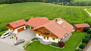 Una casa grande con techo rojo, varios portones de garaje y un camino de entrada con coches.