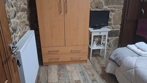 Un dormitorio con un armario de madera, una mesita blanca con un televisor y una cama con edredón blanco.