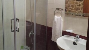 Un baño con ducha envuelta en vidrio, un lavamanos blanco y una pared de piedra.