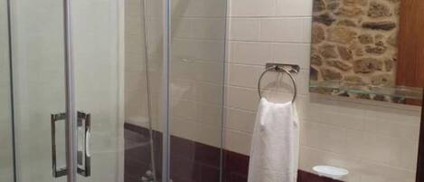 A bathroom with a glass-enclosed shower, a white sink, and a stone wall.