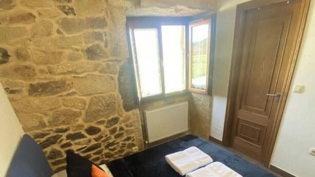Un dormitorio con pared de piedra, techo de madera, cama con ropa de cama blanco y negro, y ventana con vistas.
