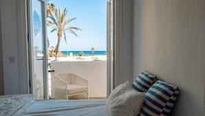 A bedroom with a bed, a view of the beach, and a chair outside.