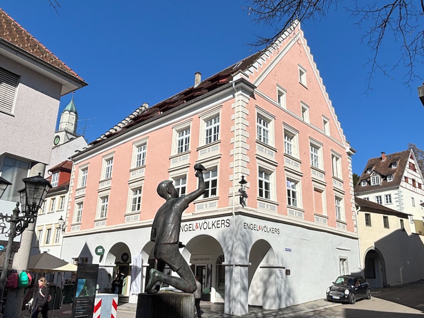 Ein pinkfarbenes Gebäude mit der Beschriftung 'Engel & Volkers', eine Statue davor und ein strahlend blauer Himmel.