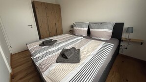 Un dormitorio con una colcha a rayas, dos almohadas, una mesita de noche con lámpara y un armario de madera.