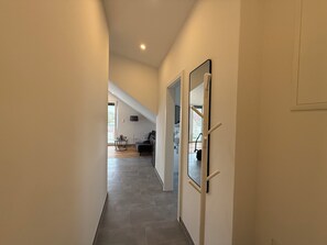 A hallway with a ceiling light, a door with a mirror, and a view into a room with a sofa and a lamp. - Simon Living - Apartment Karlsburg central and quiet location in Karlsruhe (Karlsruhe)