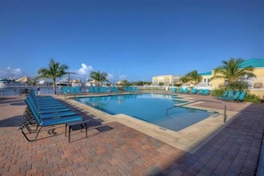 A swimming pool with lounge chairs and a brick walkway.