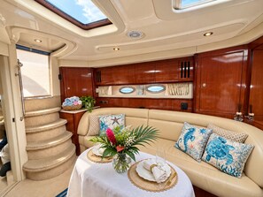 A yacht interior with a dining area, a cushioned seating area, and a staircase.