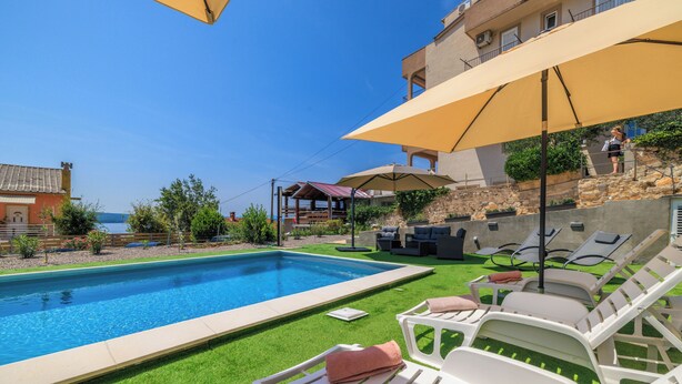 A swimming pool with lounge chairs and umbrellas, surrounded by a well-maintained lawn and a stone wall. - Apartment in Dramalj with balcony, sea view and pool (Crikvenica)