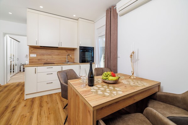 Una cocina moderna con armarios blancos, encimera de madera y zona de comedor con mesa y sillas de madera.