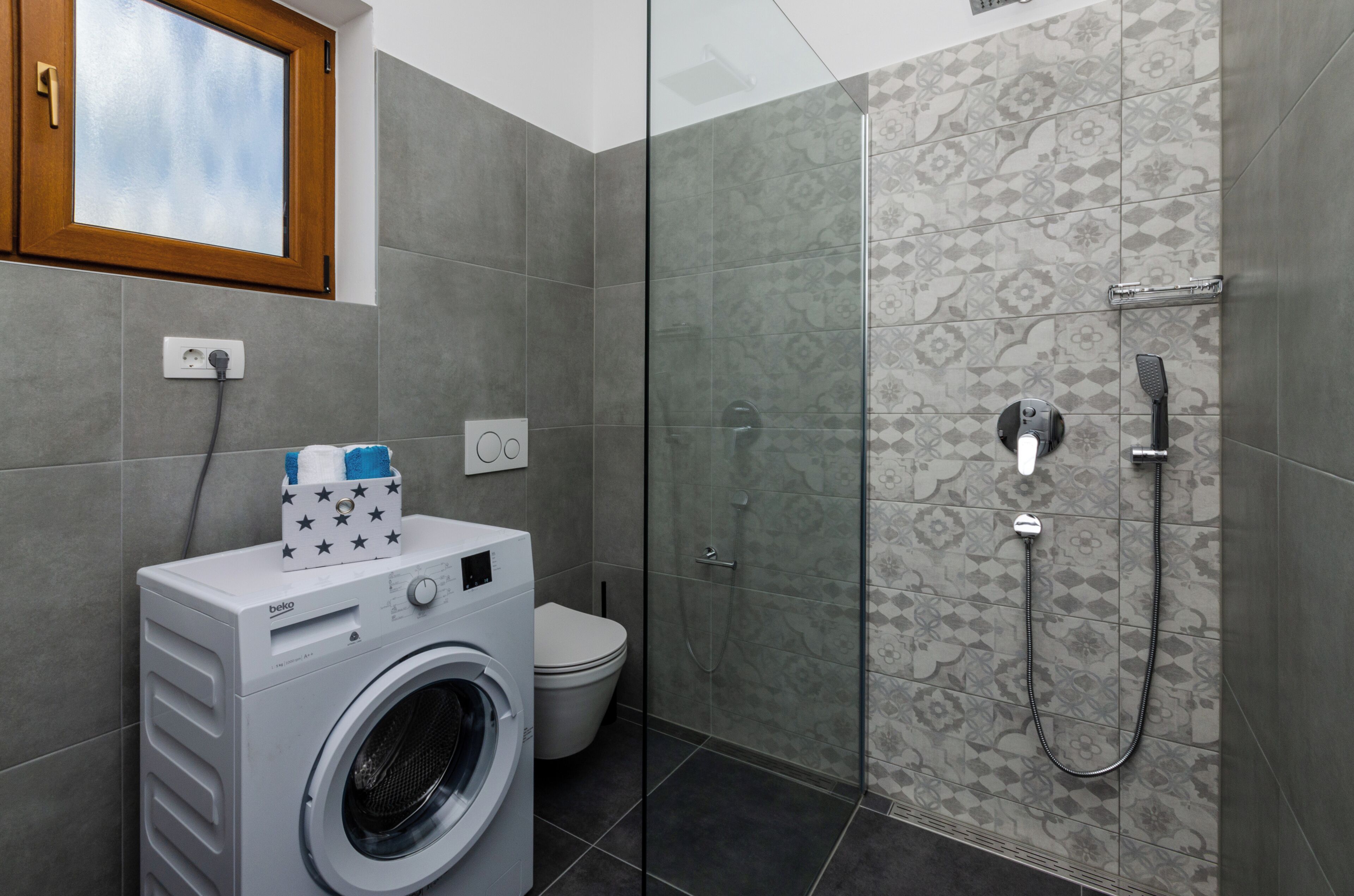 Un baño con lavadora, inodoro y zona de ducha con mampara de cristal.