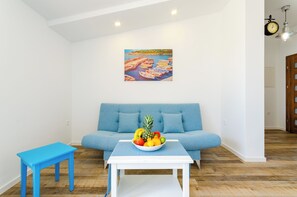 A living room with a blue sofa, a small table with a fruit bowl, and a painting of boats on the wall. - Family-friendly penthouse with sea views - just 100 m from the sandy beach (Crikvenica)