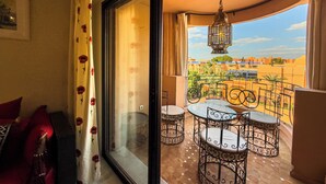 A balcony with a view of buildings, a table with chairs, and a hanging light fixture. - Stylish 2BR in L'Hivernage Pool & M'Avenue view (Marrakech)