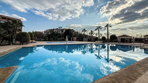 A swimming pool with clear blue water, surrounded by palm trees and buildings. - Stylish 2BR in L'Hivernage Pool & M'Avenue view (Marrakech)