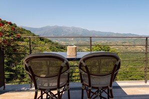 Un balcón con dos sillas de mimbre y una mesa, con vistas a un paisaje montañoso.