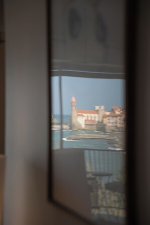 A view through a window with a building, a tower, and a body of water. - Incredible Sea View: Quiet Cocoon on the Top Floor (Collioure)