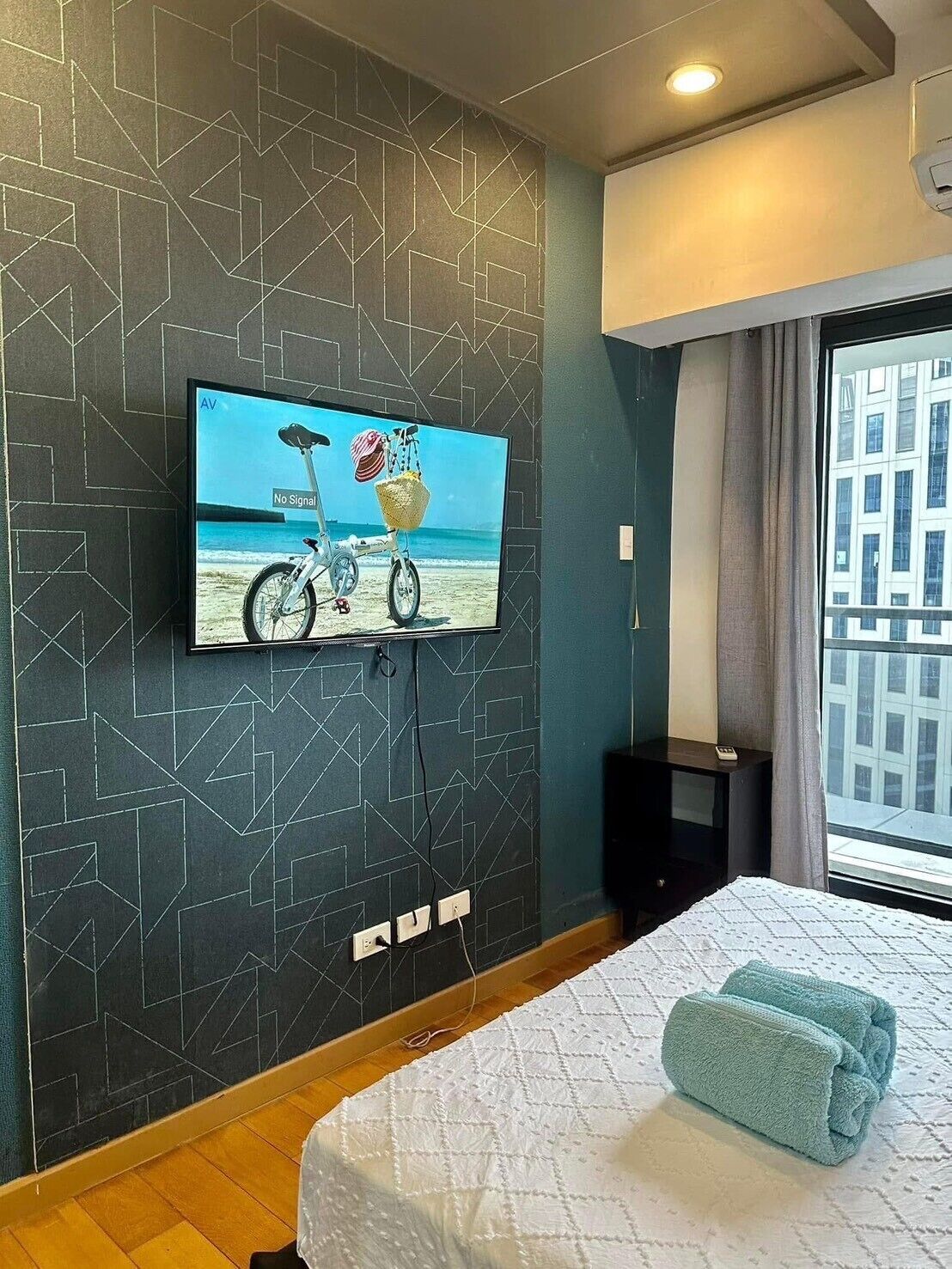 Hotelkamer met een aan de muur bevestigde televisie, een bed met een witte quilt en een raam met gordijnen.