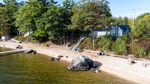 Une plage avec une maison, une eau cristalline et des arbres.