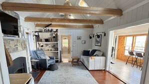 Un salon chaleureux avec une cheminée, des poutres en bois, un canapé et un coin repas avec des chaises.
