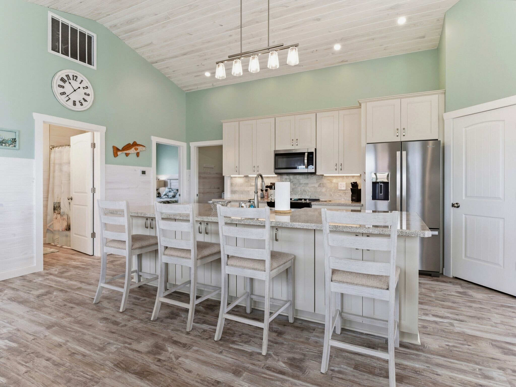 A kitchen with white cabinets, a stainless steel refrigerator, and a bar area with white bar stools.