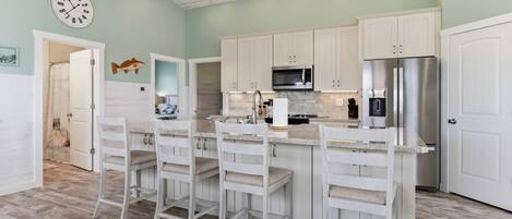 A kitchen with white cabinets, a stainless steel refrigerator, and a bar area with white bar stools.