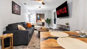 A modern living room with a sofa, coffee table, and a TV displaying 'NETFLIX'. - 3 BR Tampa Pool Home - Putting Green |Firepit |Coffee Bar (Tampa)