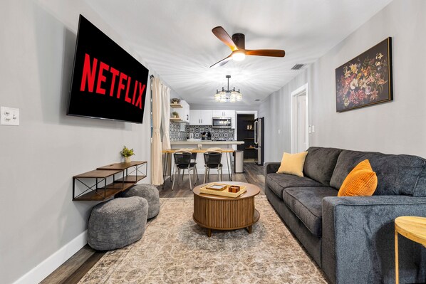 Ein modernes Wohnzimmer mit Flachbildfernseher, Deckenventilator, Essbereich und grauem Sofa.