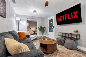 Ein modernes Wohnzimmer mit einem grauen Sofa, einem runden Couchtisch und einem großen Netflix-Schild an der Wand.