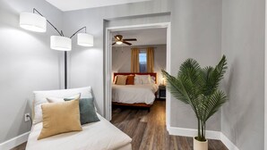 A bedroom with a bed, bedside lamps, a ceiling fan, a nightstand, a potted plant, and a view through an open door to another room. - 3 BR Tampa Pool Home - Putting Green |Firepit |Coffee Bar (Tampa)