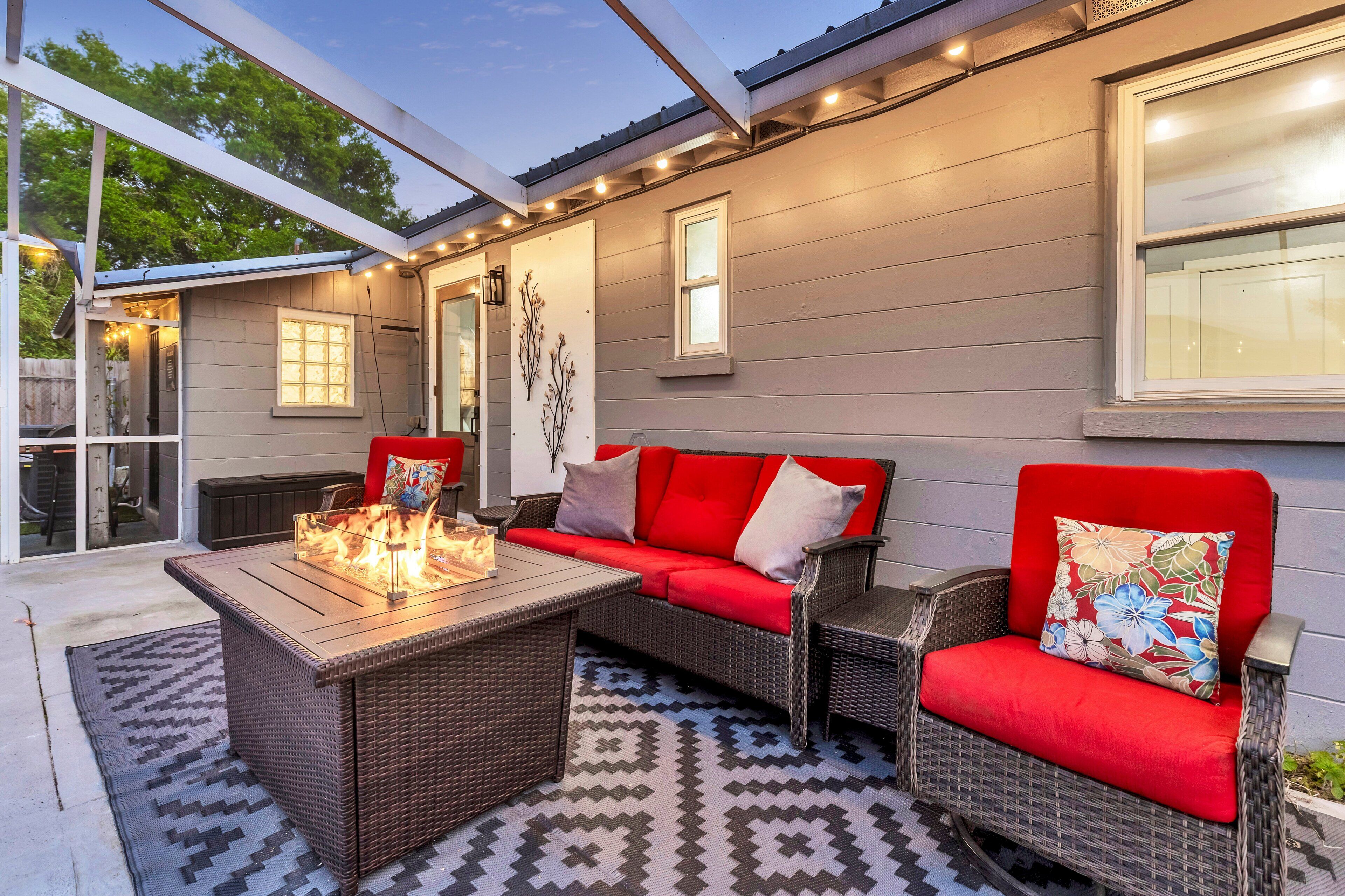 An outdoor patio with a wicker sofa, a wooden table with a fire feature, and a patterned rug.