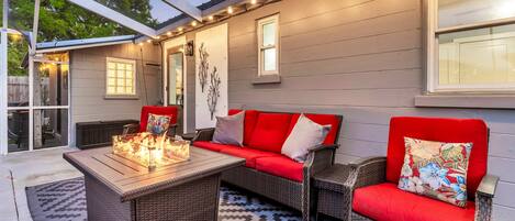 An outdoor patio with a wicker sofa, a wooden table with a fire feature, and a patterned rug.