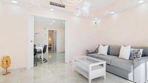 Uma sala de estar moderna com um sofá, uma mesa de centro e uma área de jantar ao fundo.