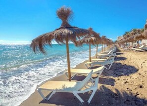 A beach with white lounge chairs and thatched umbrellas. - Marina Suites 1 | Fuengirola (Fuengirola)