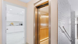 Um elevador com interior metálico, porta branca e parede com textura.