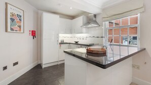 A modern kitchen with white cabinetry, a black countertop, and a window with a view of a brick building. - Boutique Living in Iconic Mayfair (London)