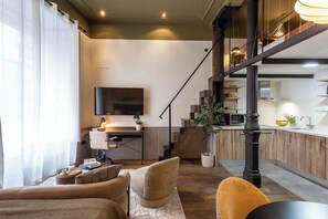 A modern living room with a sofa, a coffee table, and a TV. There is a staircase leading to an upper level. - A stylish and modern 50 m² loft in the heart of Madrid, located on the iconic Corredera Baja de San Pablo, a vibrant area brimming with theaters, restaurants, and charming cafes, just steps from Malasaña, Gran Vía, and Plaza de España. (MADRID)