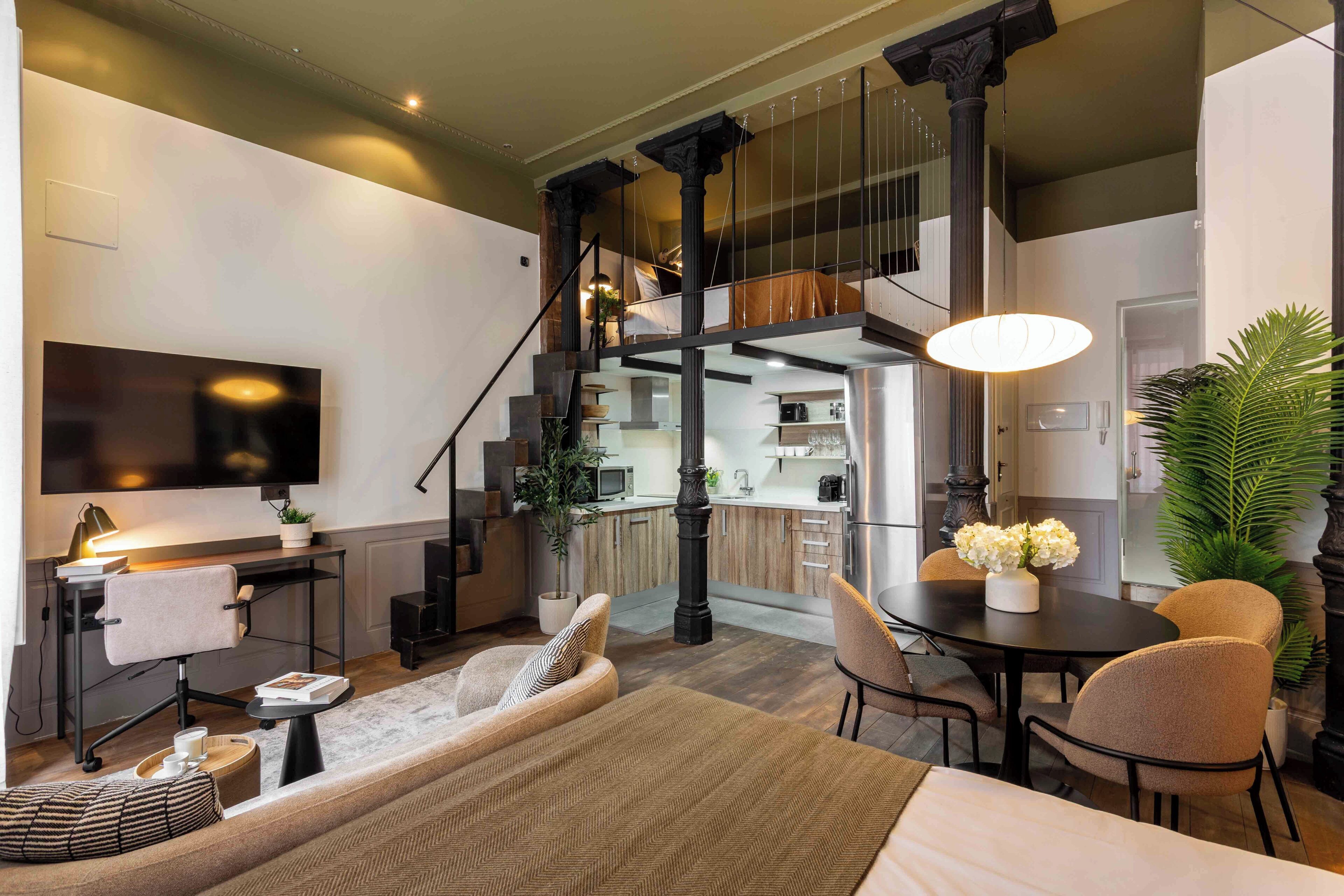 A modern living room with a sofa, coffee table, and a TV. There is a staircase leading to an upper level.