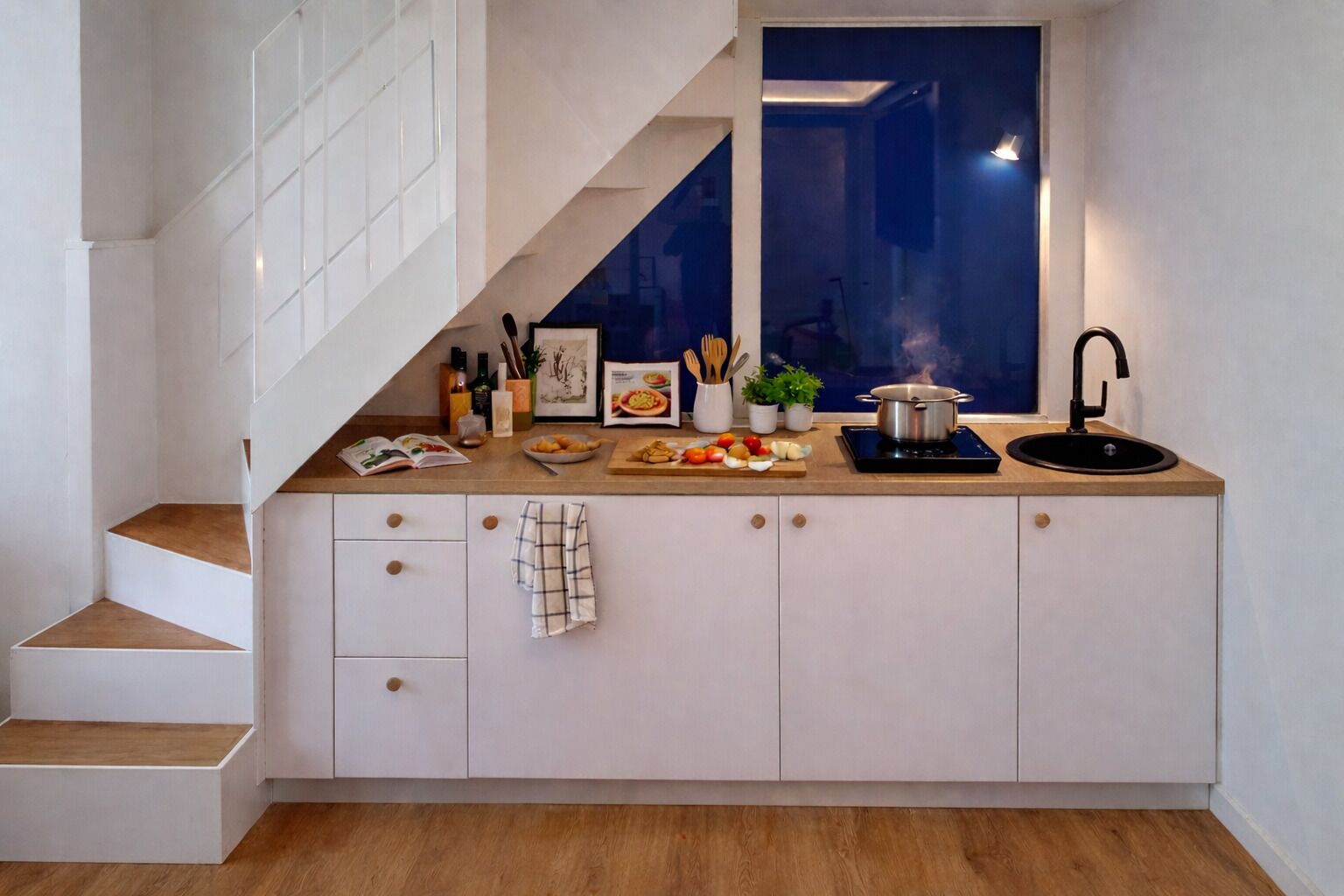 A kitchen with a built-in stove, a sink, and a window overlooking a darkened room.