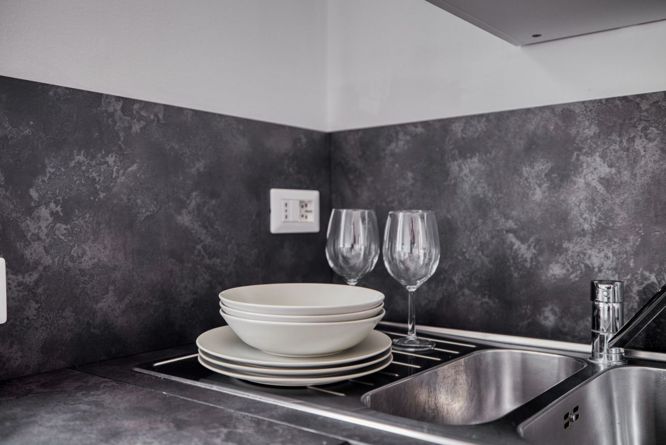 A kitchen with a stainless steel sink, a wall-mounted electrical outlet, and two wine glasses.