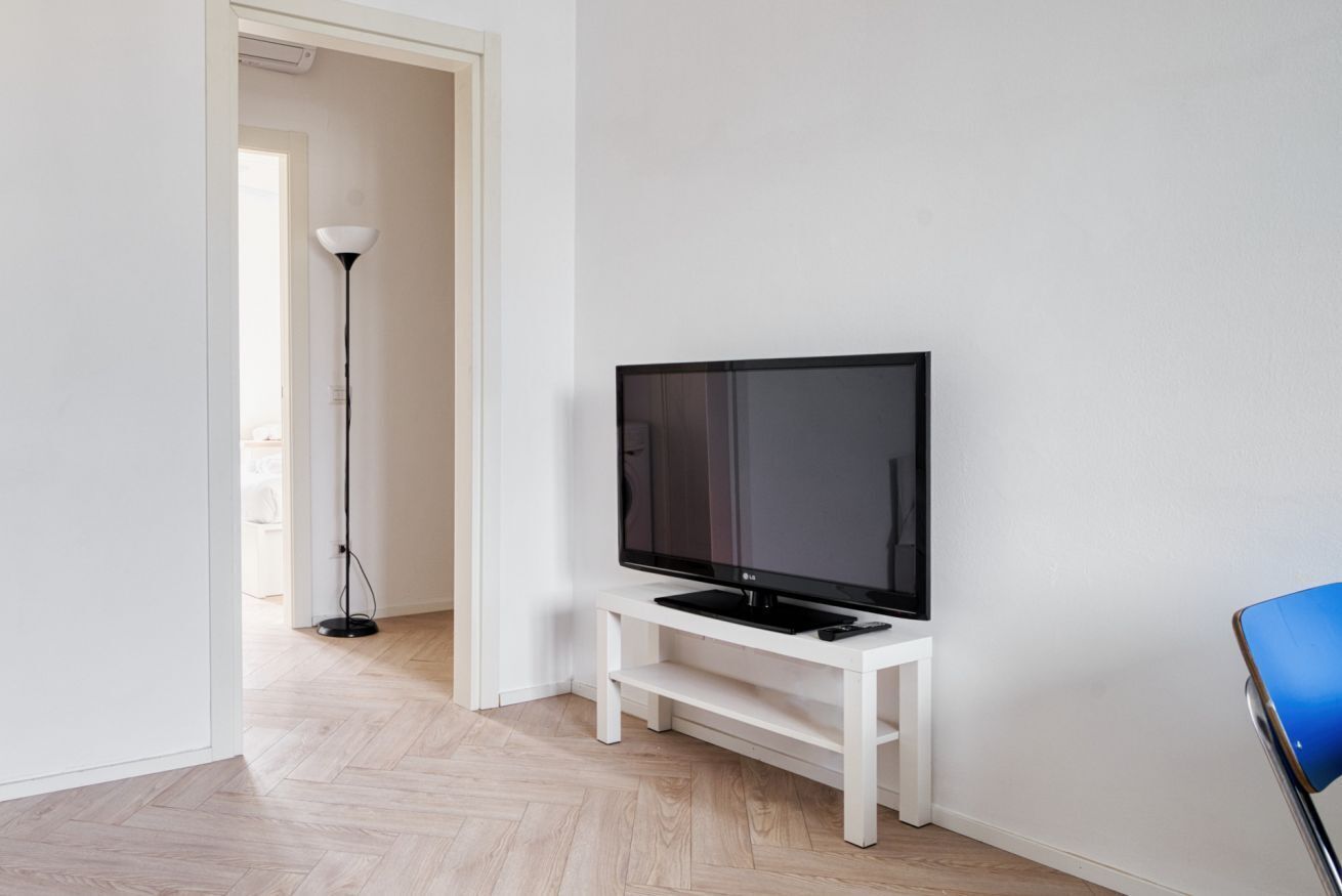 Ein Zimmer mit einem Fernseher auf einem weißen Schrank, einer Stehlampe und einem blauen Stuhl.