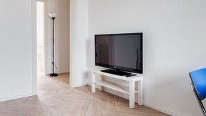 Una stanza con una televisione su un supporto bianco, una lampada da terra e una poltrona blu.