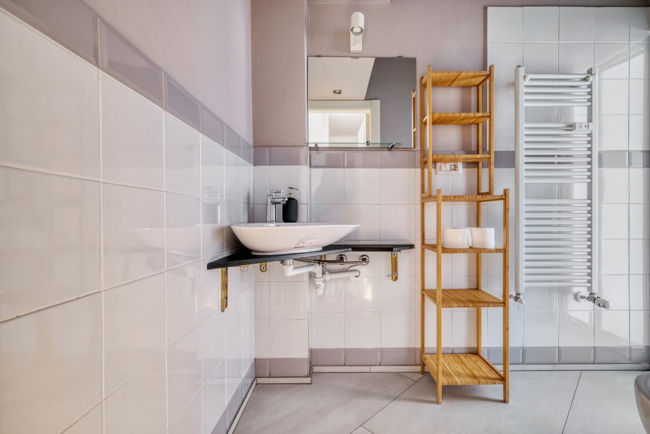 Un baño moderno con un lavabo sobre encimera, un estante de madera y un perchero para toallas.