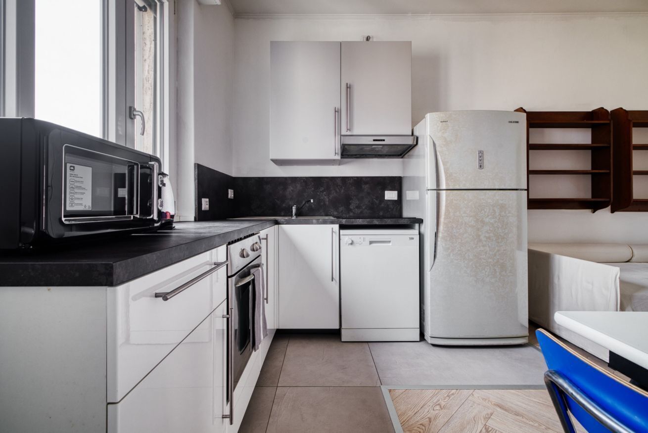 Eine moderne Küche mit weißen Schränken, einer schwarzen Arbeitsplatte, einem Einbauofen, einem Geschirrspüler und einem Kühlschrank.