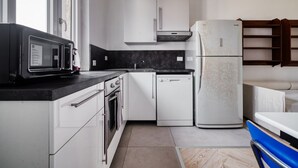 Una cucina moderna con mobili bianchi, un piano di lavoro nero, forno a incasso, lavastoviglie e frigorifero.