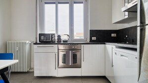 Una cucina moderna con mobili bianchi, forno integrato, macchina da caffè e finestra sopra il lavello.